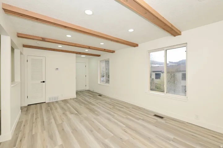 Spacious room featuring wood-finish flooring, exposed ceiling beams, recessed lighting, white walls, and a large window