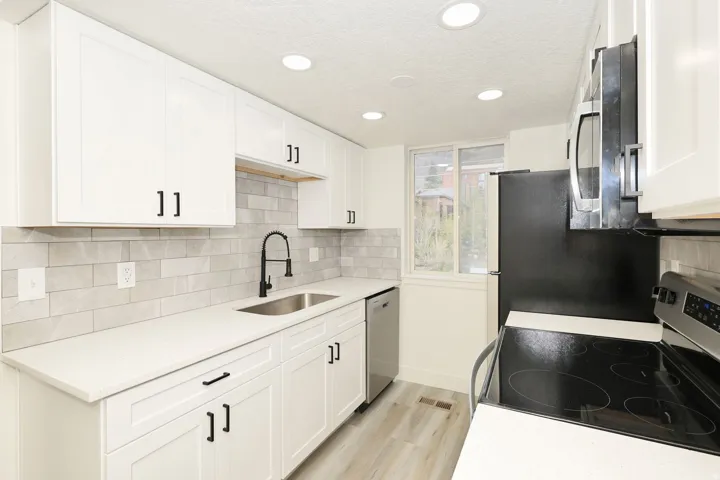 Modern kitchen featuring white shaker cabinetry with matte black hardware, light grey subway tile backsplash, white countertops, and stainless steel appliances