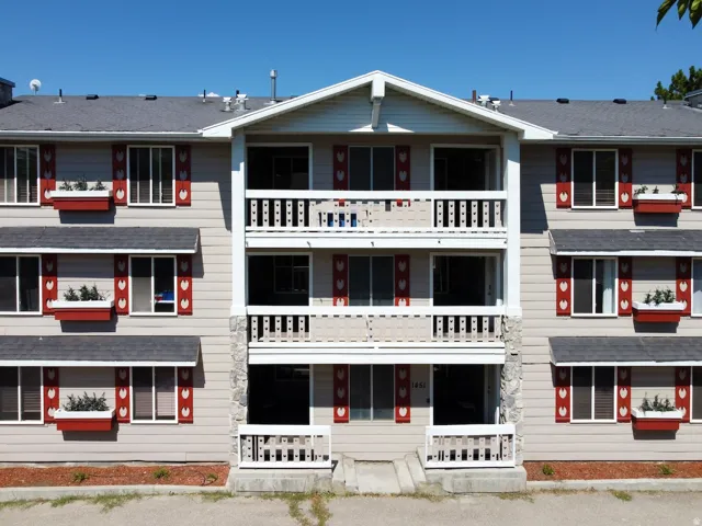 Multi-story building featuring light-colored siding, a dark shingle roof, and white-railed balconies/patios