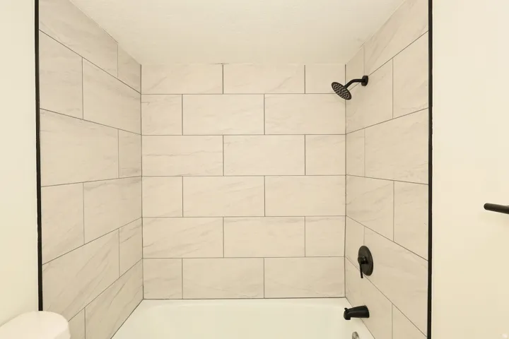 Bathtub-shower combination featuring light-toned tile surround, matte black shower head, and coordinating matte black fixtures