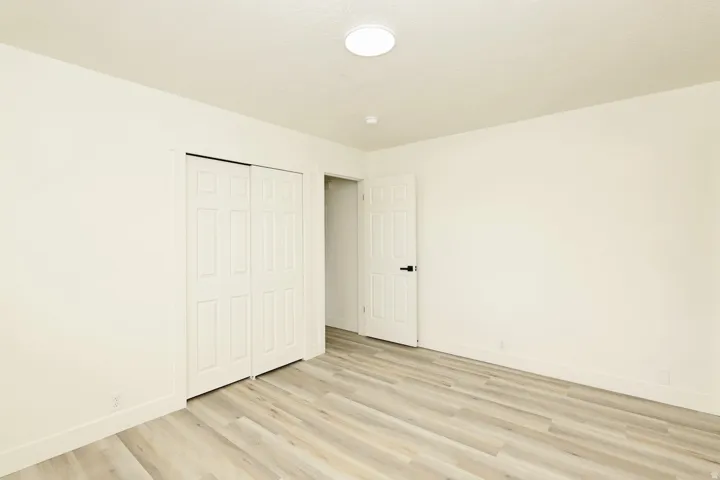 Spacious room featuring light wood-finish flooring, white walls, and a ceiling-mounted flush light fixture