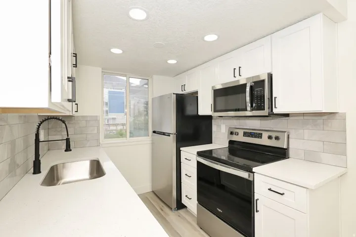 Modern kitchen featuring white shaker cabinetry, stainless steel appliances, light-toned countertops, a subway tile backsplash, and recessed lighting