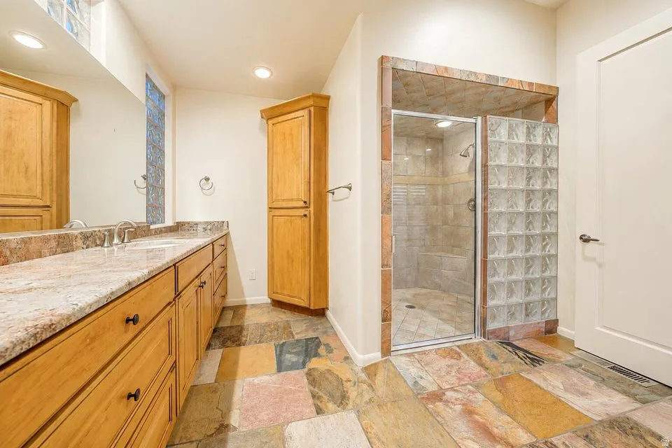 Double vanity with light-toned countertop, wood-finish cabinetry, and recessed lighting