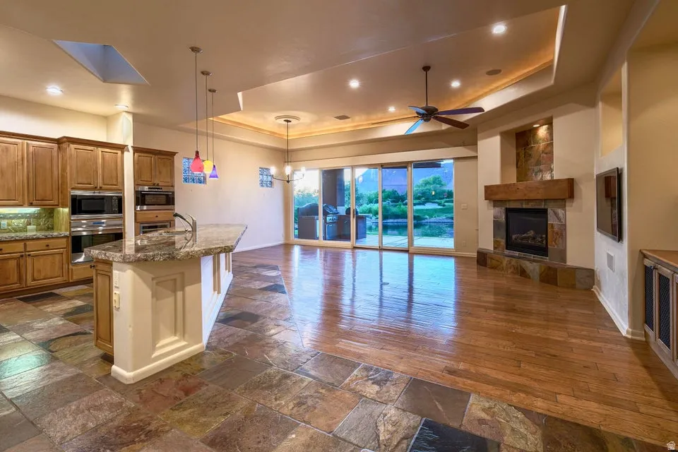 Kitchen island with a granite countertop, built-in double oven, wood-finish flooring, stone fireplace with a wood mantle, and sliding glass doors