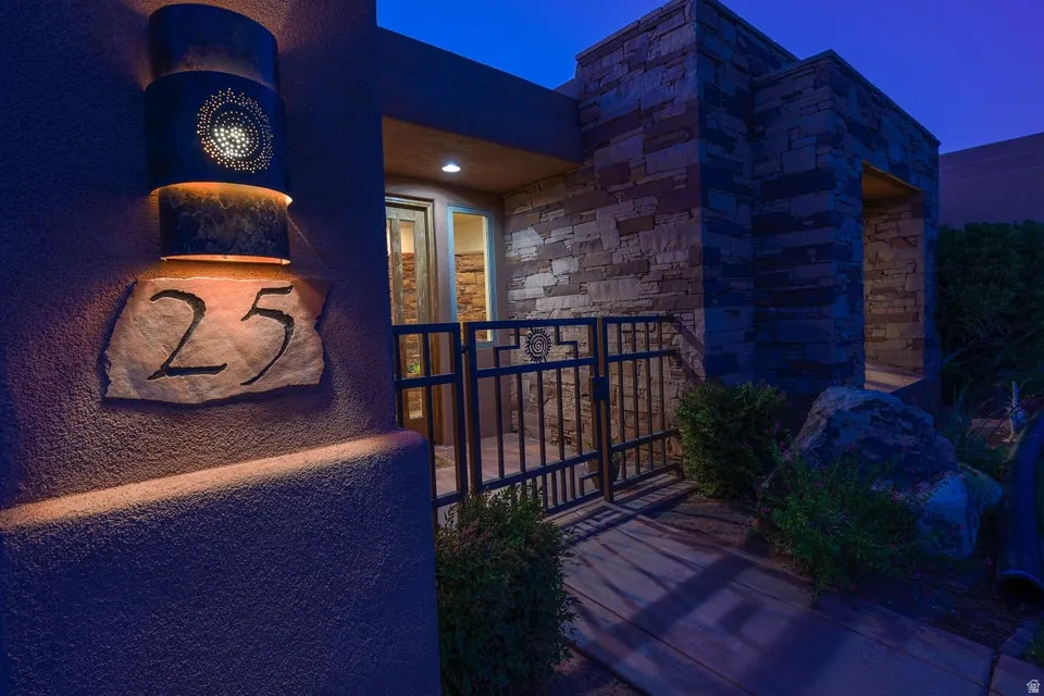 Stone veneer exterior with a decorative wall-mounted light fixture, custom wrought iron gate, and natural stone address marker