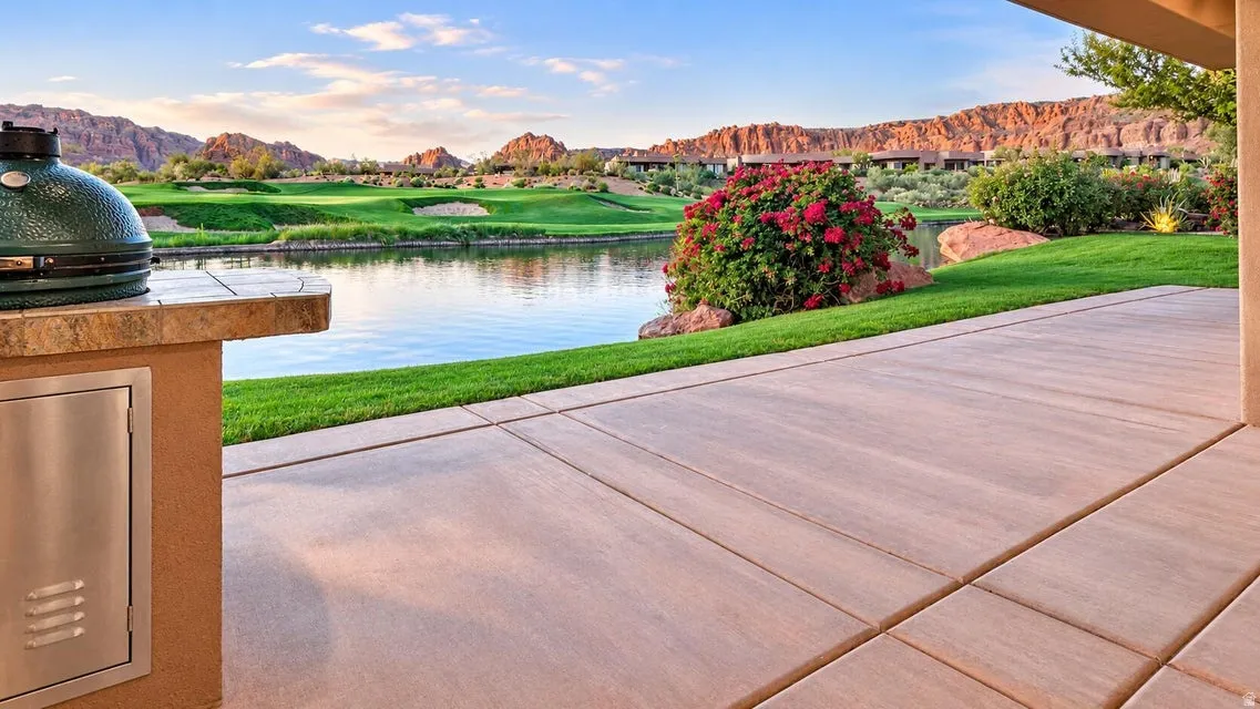 Expansive outdoor patio with large format pavers, an integrated outdoor grill station with stone countertop, overlooking a body of water and manicured golf course
