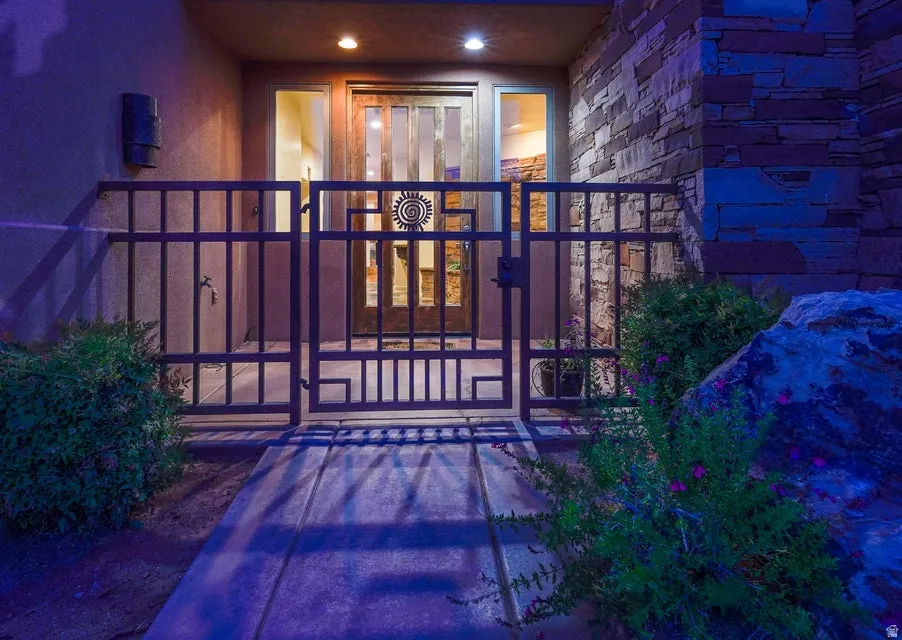 Wrought iron entry gate, stacked stone wall accent, prominent rock landscaping, stucco exterior, and transom window