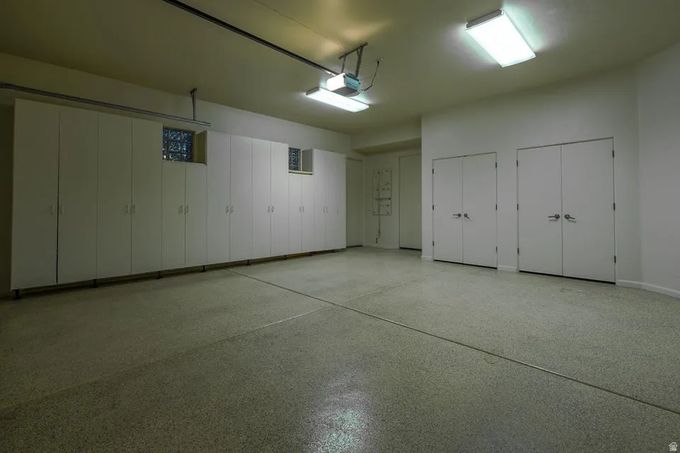 Expansive garage featuring a speckled epoxy floor, extensive built-in cabinetry, dual flush-mount fluorescent lighting, and two sets of double-door storage