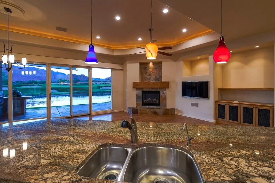 Granite countertop with dual stainless steel sinks, floor-to-ceiling sliding glass doors, built-in fireplace with stone surround, wood-finish flooring, and recessed ceiling lighting