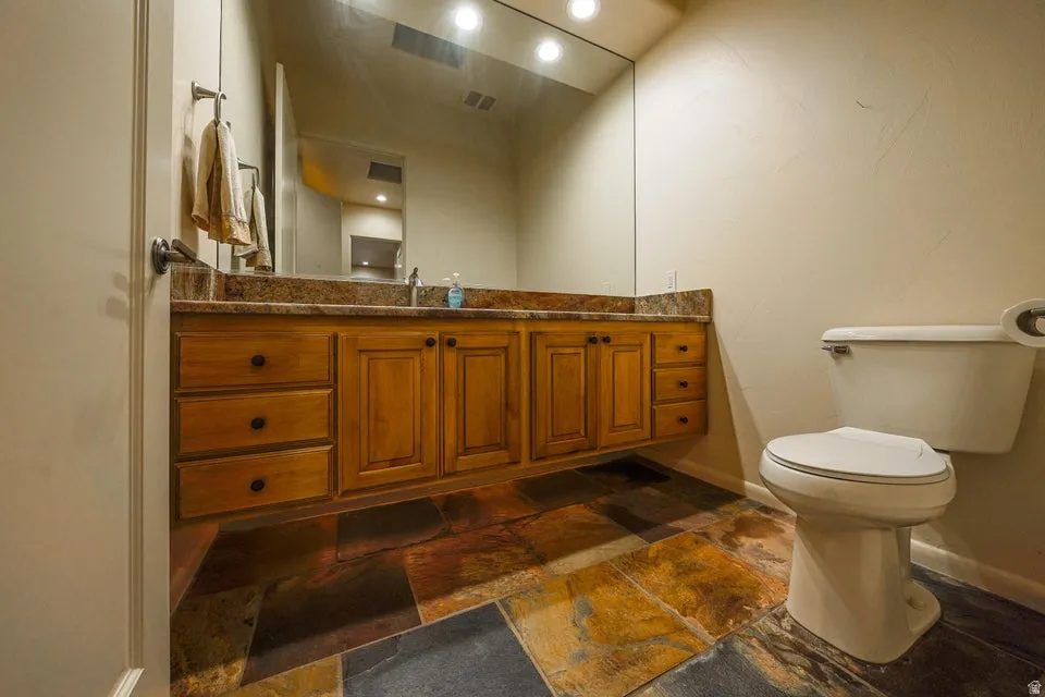 Floating wood-finish vanity with a stone countertop, featuring an integrated mirror and flagstone flooring