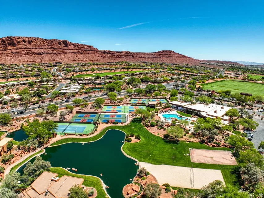 Expansive community featuring multiple tennis courts, a swimming pool, a volleyball court, and a tranquil pond, all set against a desert landscape with a prominent rock formation