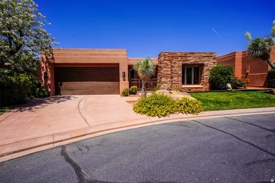 Stucco exterior with stone accents, integrated garage, paved driveway, and manicured landscaping