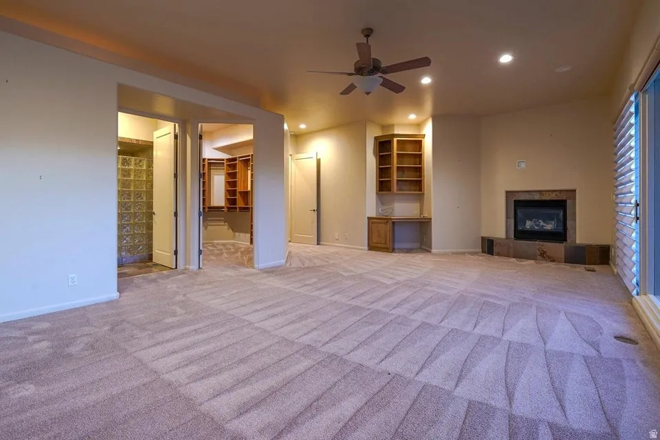 Spacious room featuring patterned carpeting, built-in shelving with a desk, and a fireplace with a stone surround