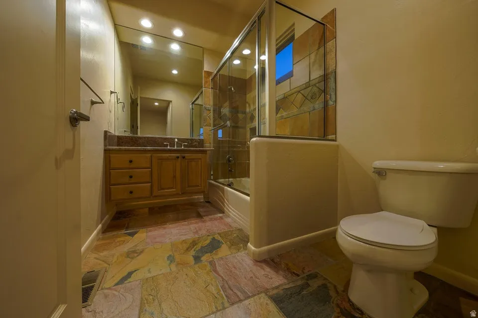 Full bathroom featuring a single vanity with a stone countertop, a shower-tub combination with a glass enclosure, and a natural stone tile floor
