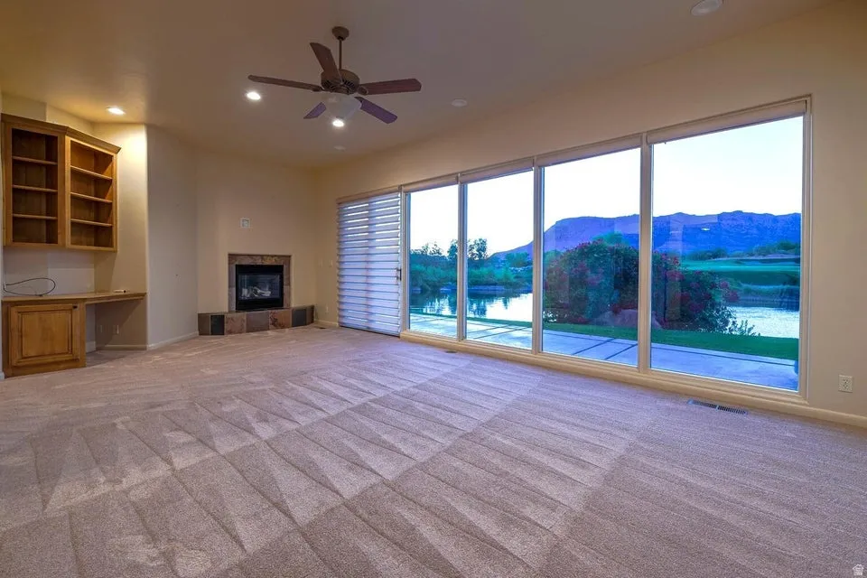 Extensive floor-to-ceiling windows, built-in shelving with desk, fireplace with stone surround, and recessed lighting
