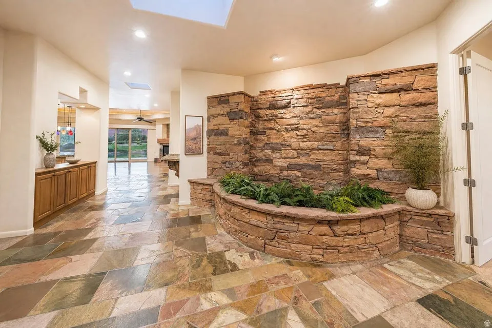 Expansive stone flooring with a natural stone accent wall featuring an integrated planter, skylight, and recessed lighting