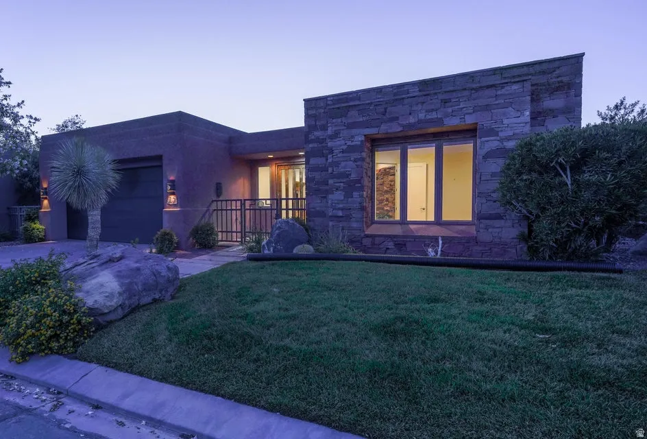 Contemporary architecture with stone and stucco exterior, prominent window with dark framing, metal entry gate, and an attached garage with exterior wall sconces