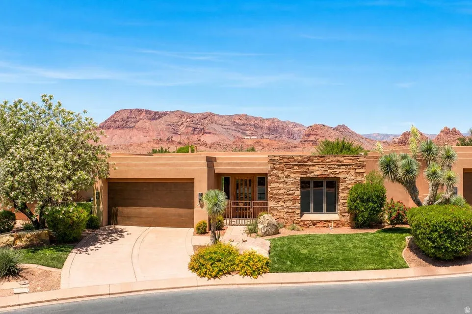 Terracotta-toned exterior featuring a stone accent wall, an integrated garage, a manicured lawn, and native desert landscaping