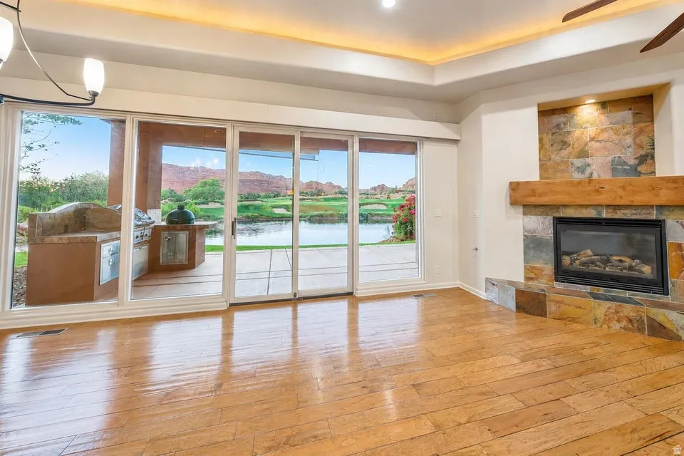Wood-finish flooring, a stone-clad fireplace with a wood mantle, and sliding glass doors leading to an outdoor kitchen area