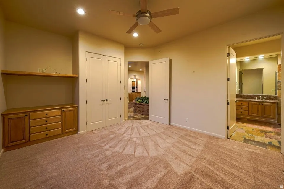 Recessed lighting, ceiling fan, built-in wooden cabinetry, double-door closet, and an attached bathroom with a dual vanity