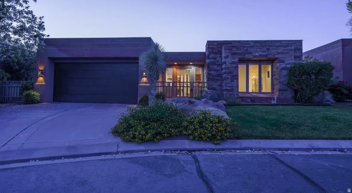 Contemporary exterior featuring a stone facade, stucco finish, attached garage with a dark door, and front landscaping with shrubs and lawn