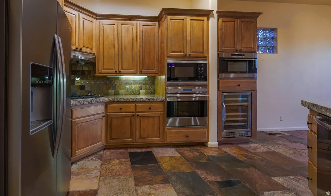 Stainless steel refrigerator, built-in microwave, wall oven, beverage cooler, and wood cabinetry with stone countertops