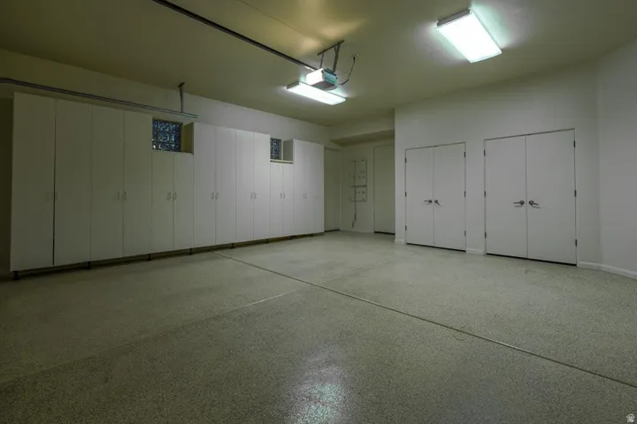 Expansive garage featuring a speckled epoxy floor, extensive built-in cabinetry, dual flush-mount fluorescent lighting, and two sets of double-door storage