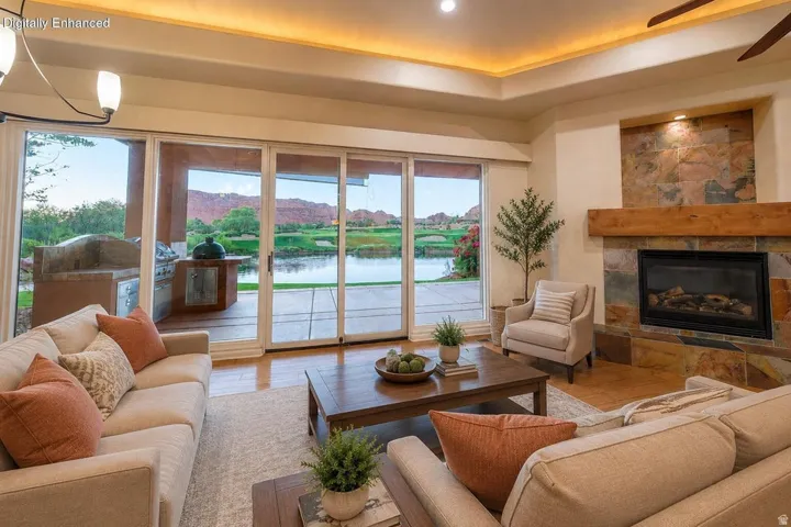 Sliding glass doors opening to an outdoor kitchen and water feature, natural stone fireplace with a substantial wood mantel, coffered ceiling with recessed lighting, and wood-finish flooring