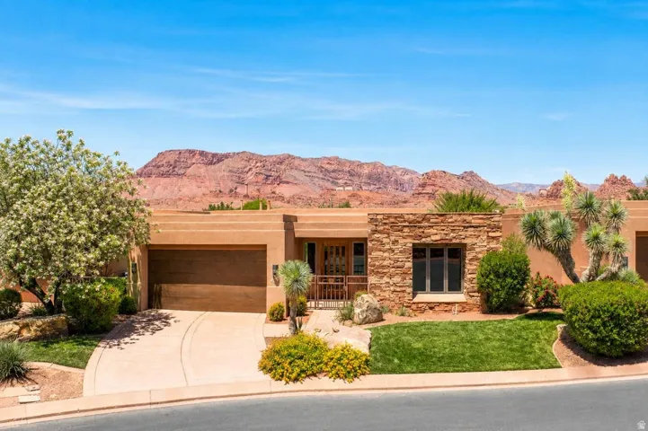 Terracotta-toned exterior featuring a stone accent wall, an integrated garage, a manicured lawn, and native desert landscaping