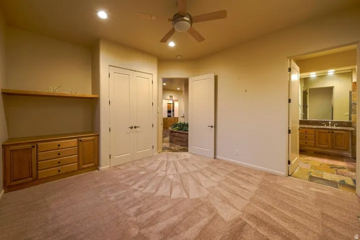 Recessed lighting, ceiling fan, built-in wooden cabinetry, double-door closet, and an attached bathroom with a dual vanity