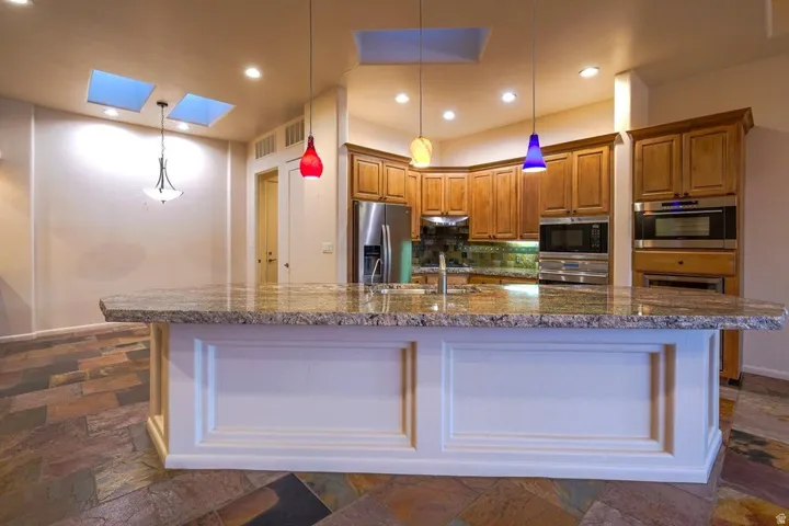 Expansive kitchen island with a stone countertop, built-in stainless steel appliances, wood cabinetry, and slate-style flooring