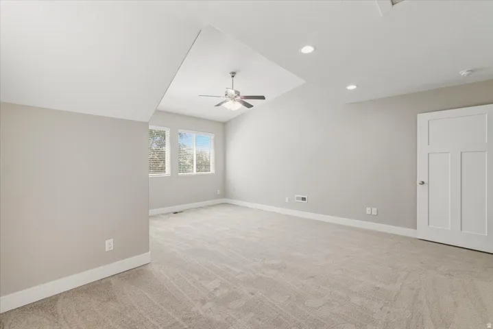 Spacious room featuring neutral carpeting, a ceiling fan, recessed lighting, and multiple windows with blinds