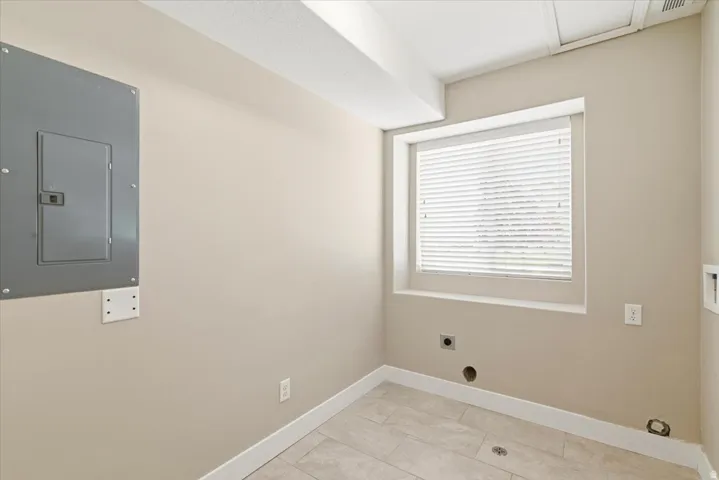 Compact utility space featuring a window with blinds, light beige wall paint, white baseboards, and tile flooring.