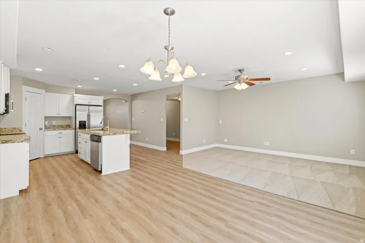 Open-concept living area featuring a kitchen with white cabinetry and granite countertops, stainless steel appliances, and a central island with a sink
