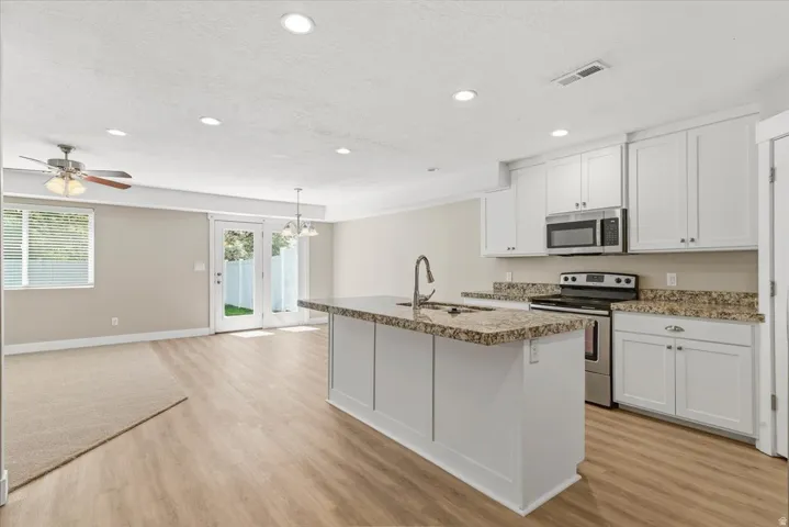 Kitchen and living area featuring wood-finish flooring, white cabinetry, a kitchen island with seating, stainless steel appliances, and recessed lighting