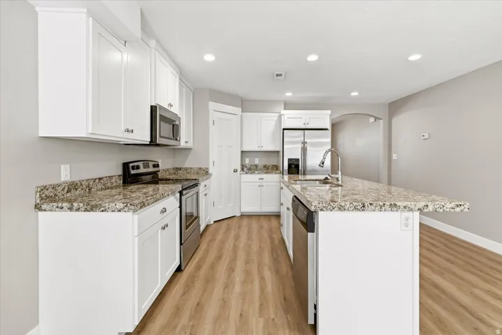 Modern kitchen featuring white cabinetry, granite countertops, stainless steel appliances, wood-finish flooring, and recessed lighting