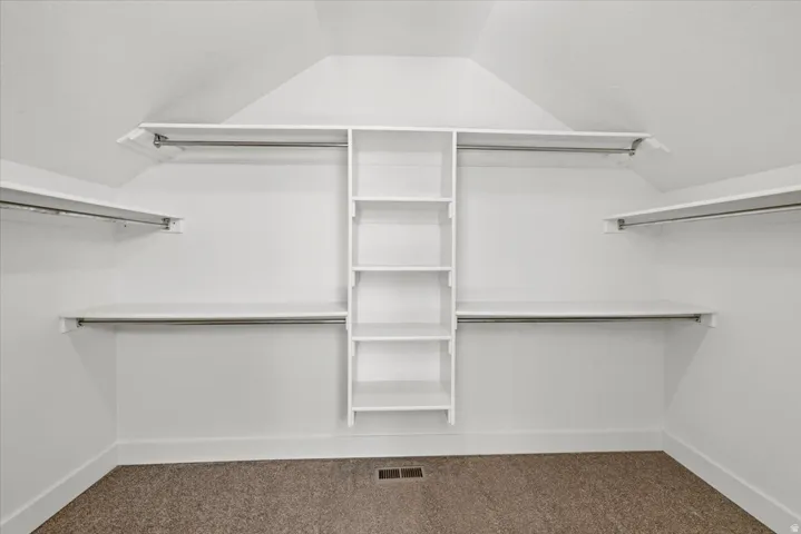 Master closet featuring extensive built-in shelving, multiple hanging rods, white trim, and neutral carpeting