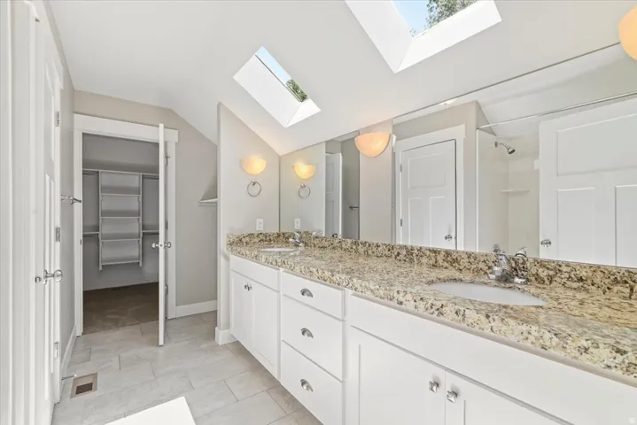 Master bath. Double vanity with granite countertop and integrated sinks, white cabinetry, tile flooring, two skylights, and sconce lighting