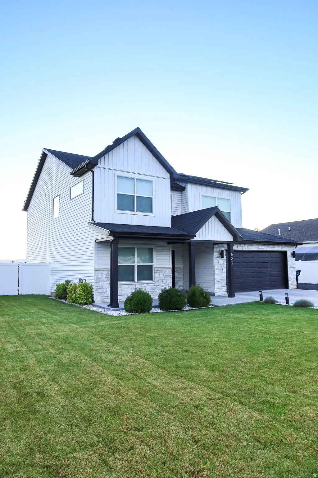 Contemporary two-story exterior featuring white vertical and horizontal siding, black trim accents, a two-car garage, and stone veneer detailing on the front facade