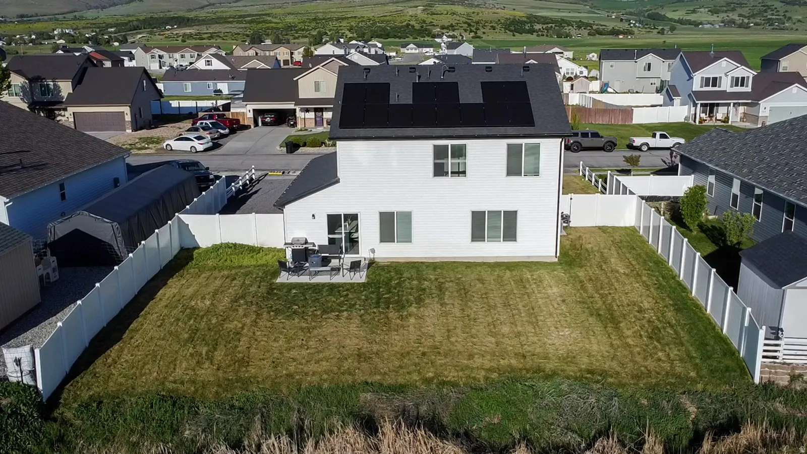 Rear exterior featuring a white siding finish and a dark shingle roof with integrated solar panels. Features Water.
