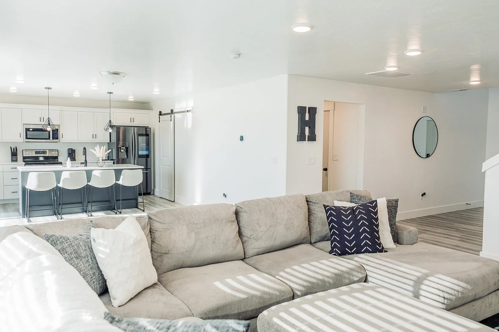 Open-concept living area featuring light wood-finish flooring, recessed lighting, a modern kitchen with a large island, stainless steel appliances, and white cabinetry