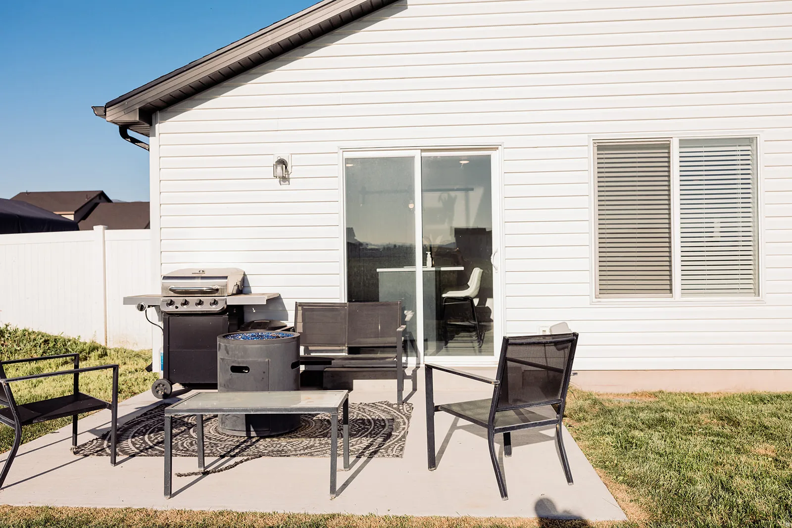 Concrete patio with white siding exterior, featuring a sliding glass door, an exterior wall sconce, and a white privacy fence