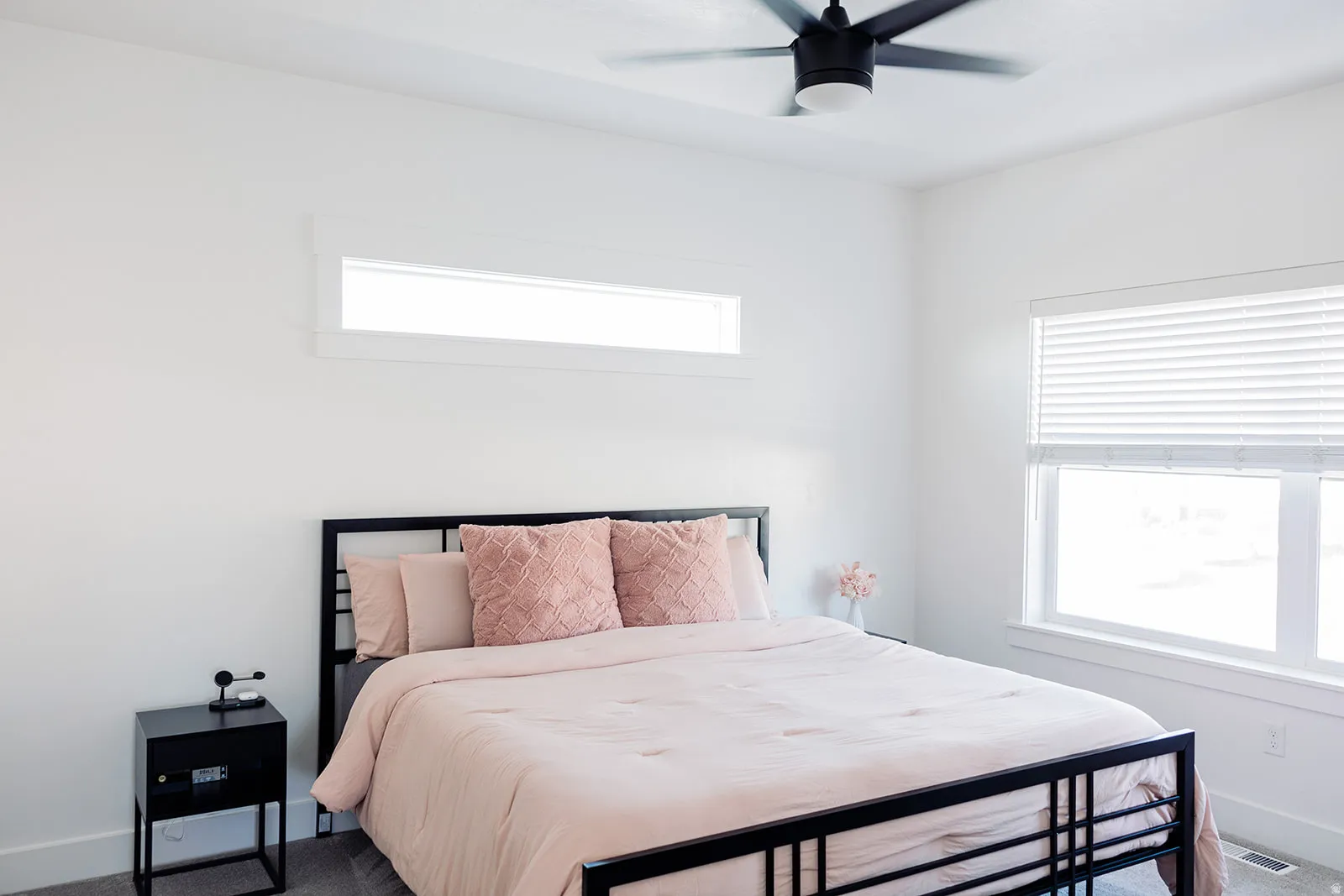 Bright bedroom featuring a large window with blinds, an upper horizontal window, a ceiling fan, and carpet flooring