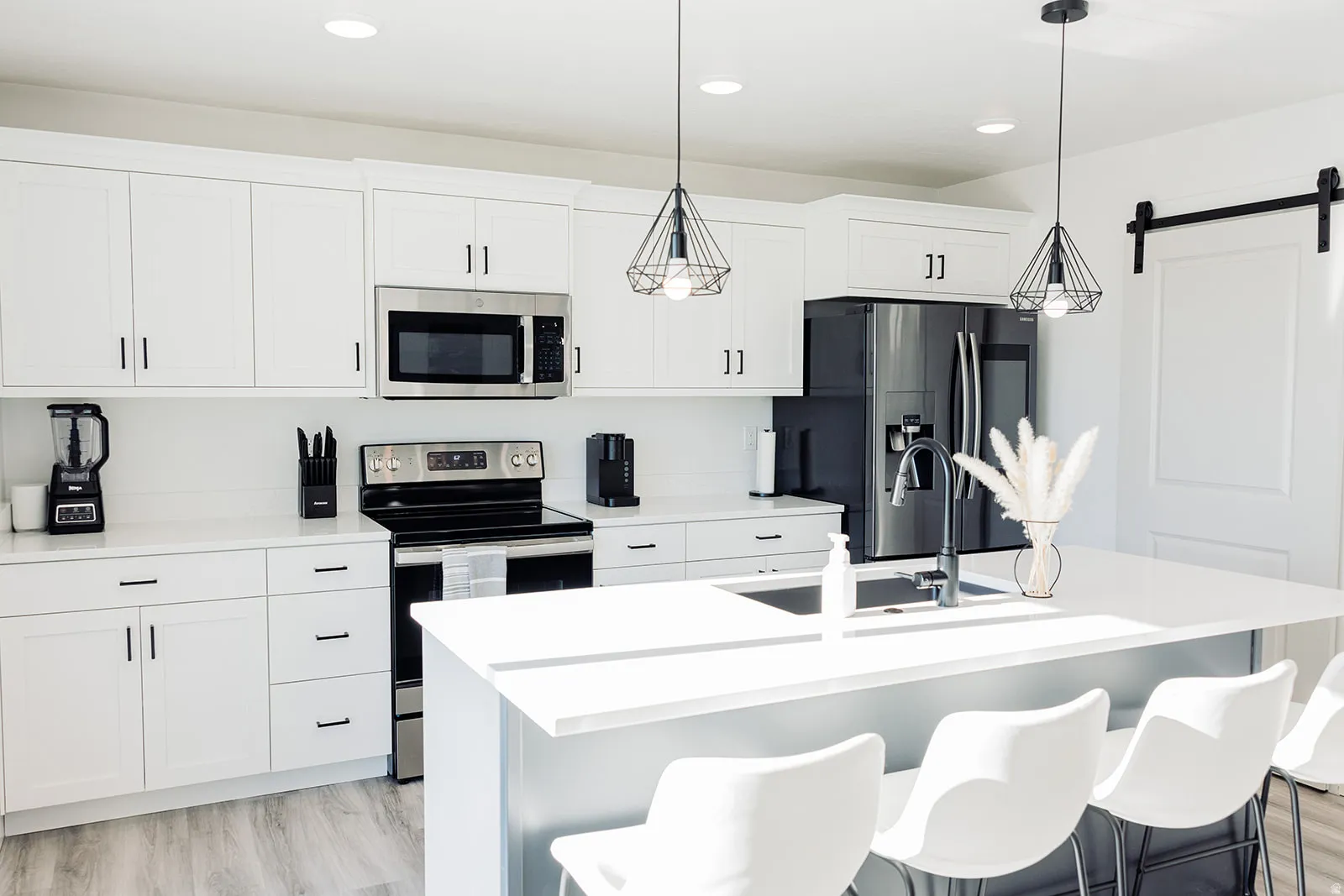 Kitchen featuring white cabinetry, stainless steel appliances, a center island with sink, pendant lighting, and wood-finish flooring