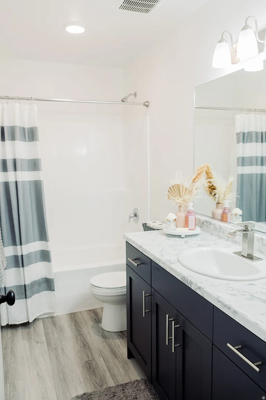 Bathroom featuring a dark wood-finish vanity with a white countertop and integrated sink, a white bathtub with an overhead shower, and wood-finish flooring