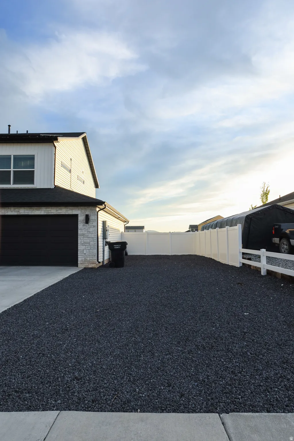 Modern siding facade with stone veneer accents, a dark garage door, and an expansive gravel side yard