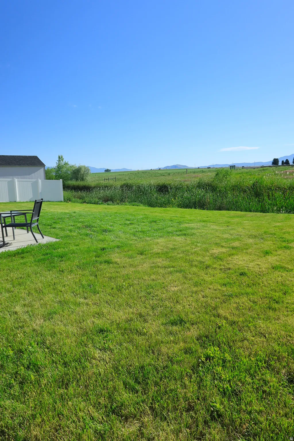 Expansive lawn with a concrete patio, bordered by a white privacy fence