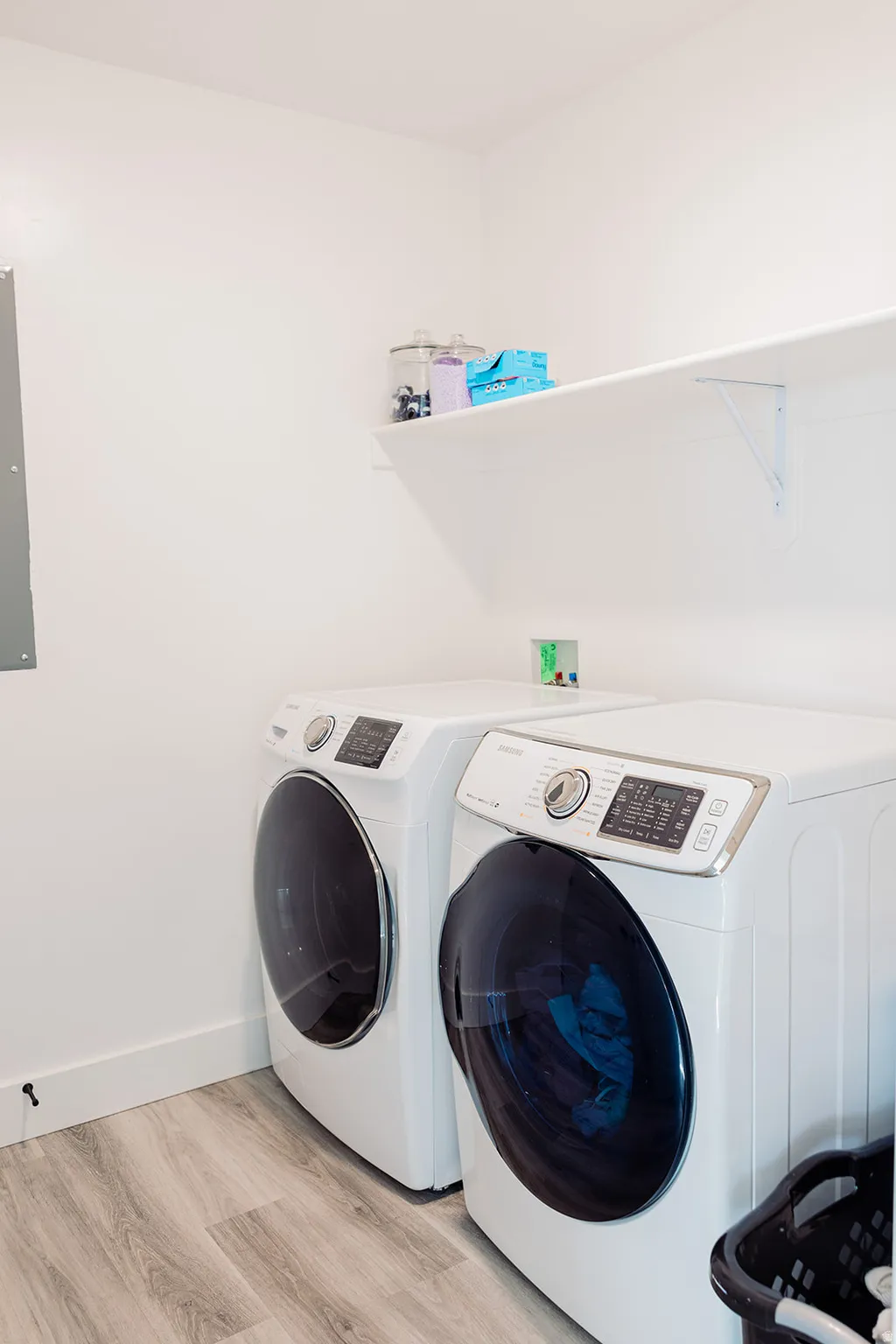 Dedicated laundry space featuring wood-finish flooring and a wall-mounted white shelving unit