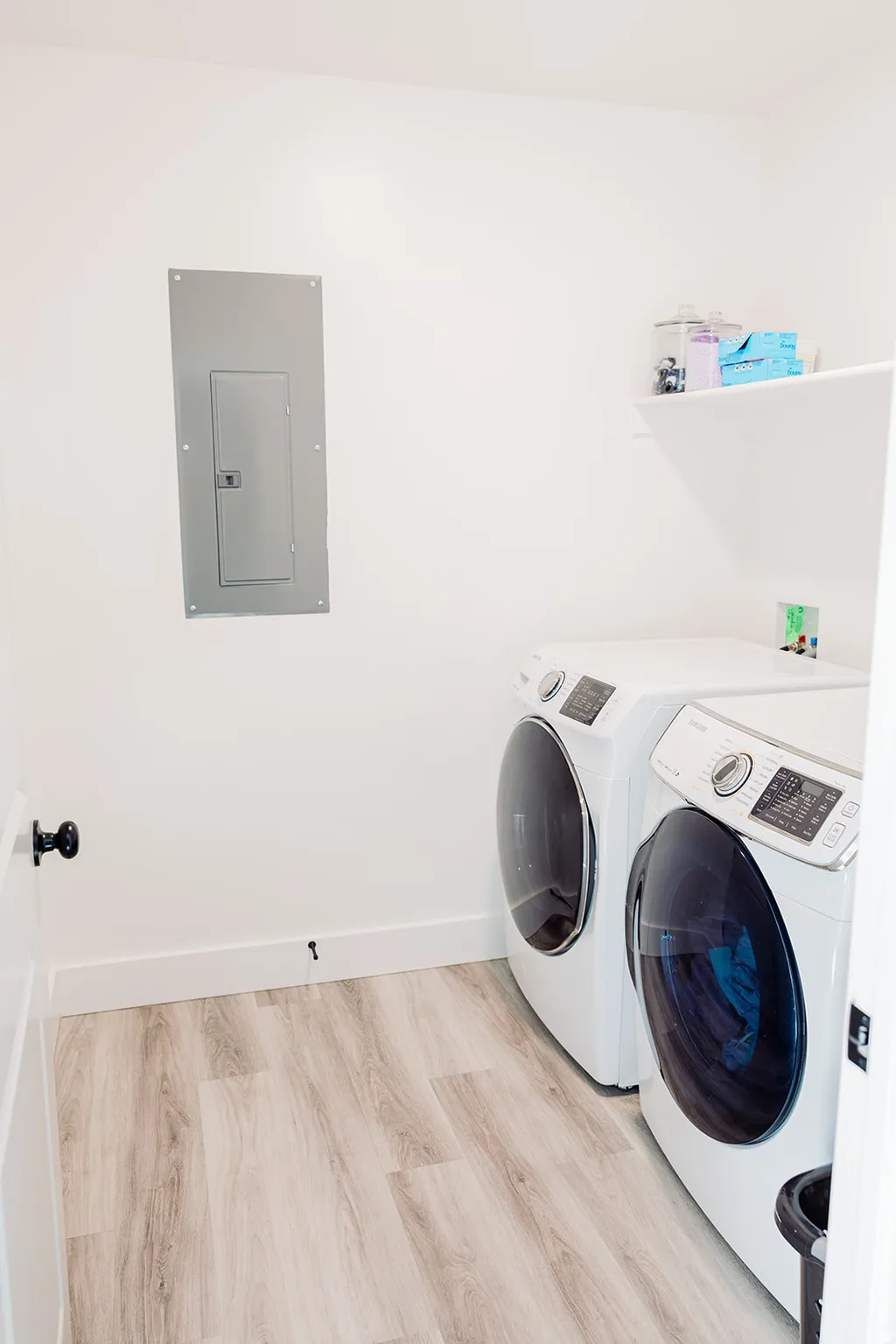 Laundry area featuring a wall-mounted shelf, light wood-finish flooring, and white baseboards