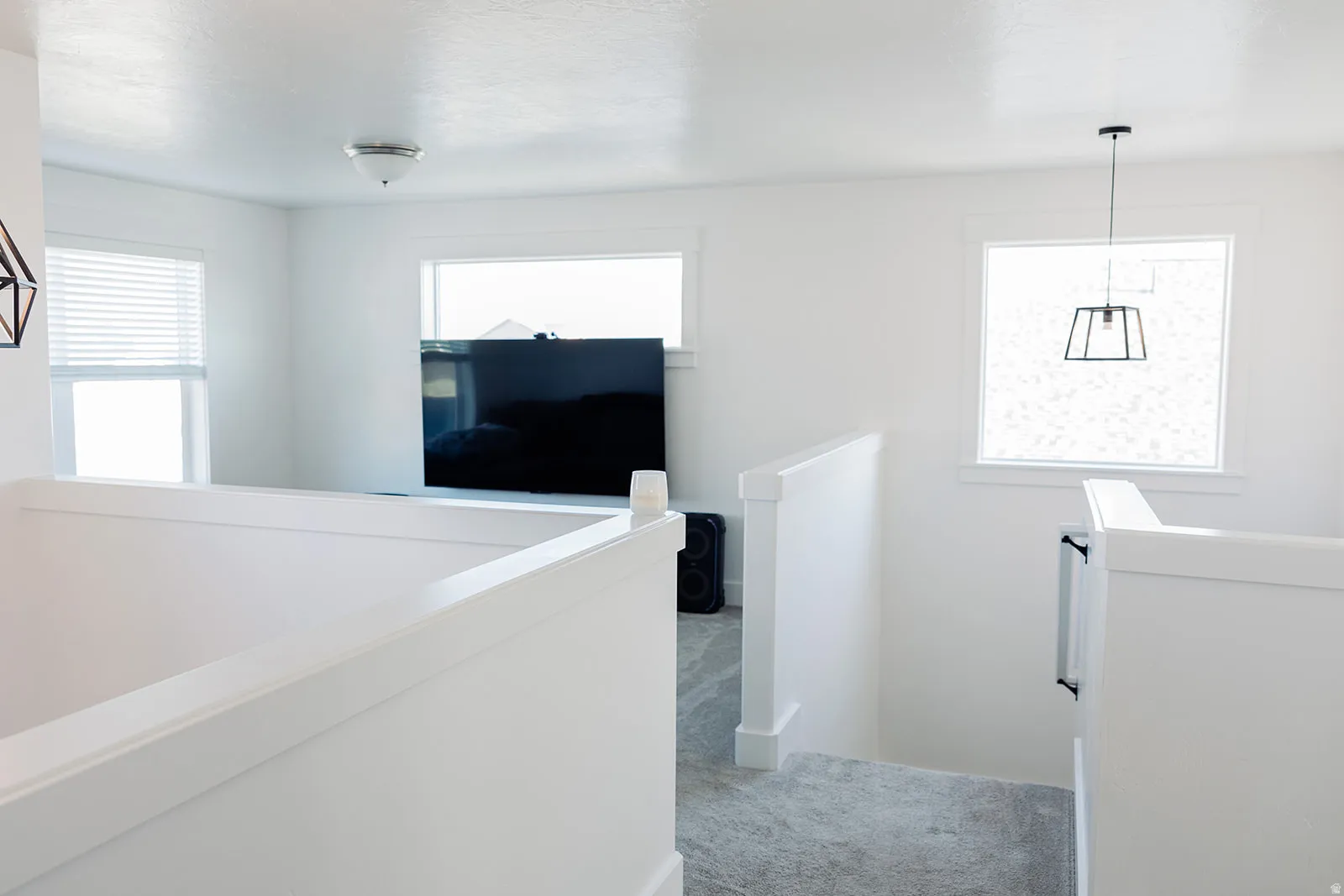 Bright upper-level landing featuring white walls, light gray carpet, and multiple windows
